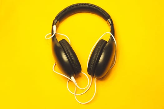 Black headphones with white cable on a yellow background. modern earphones