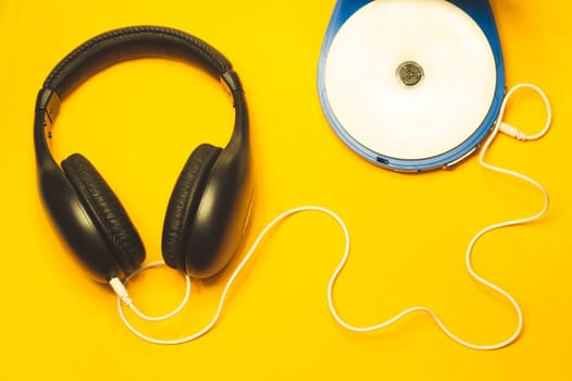 Black headphones with a white cable on a yellow background. compact disc player with white cd and earphones