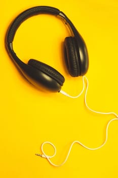 Black headphones with white cable on a yellow background. modern earphones