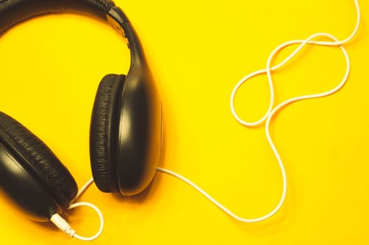 Black headphones with white cable on a yellow background. modern earphones