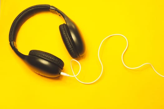 Headphones with white cable on a yellow background. black earphones