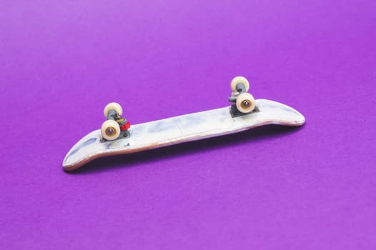 Small skateboard on purple background. tiny skate for fingers. fingerboard close up. copy space