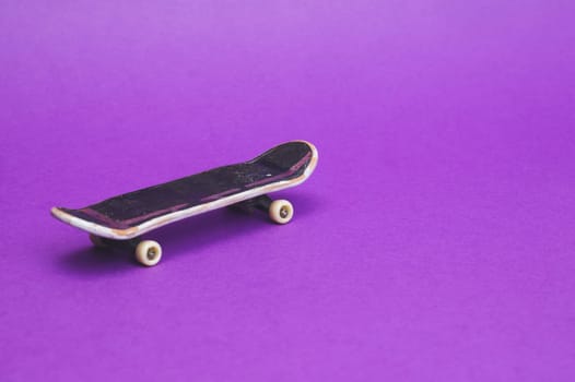 Small skateboard on purple background. tiny skate for fingers. fingerboard close up. copy space
