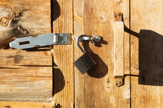 Metal padlock on a wooden door with opened latch
