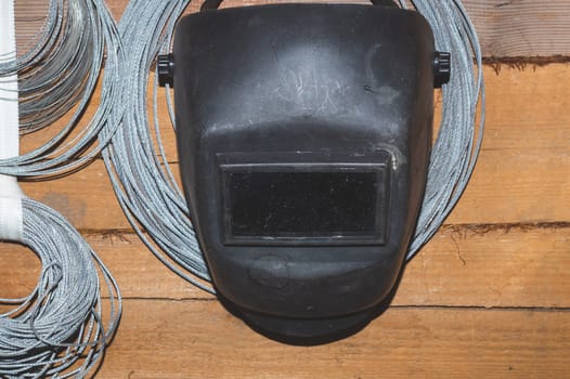 Protective welding mask hanging on a wooden wall. hanks of steel rope. helmet for ironworker