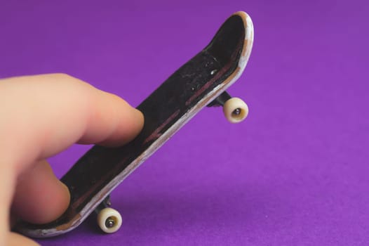 Small skateboard on purple background. fingers on tiny skate. playing with fingerboard. home leisure concept. copy space