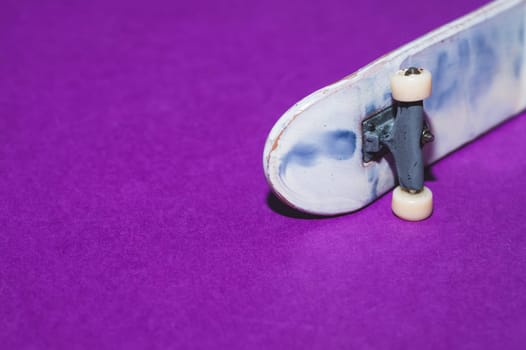 Small skateboard on purple background. tiny skate for fingers. fingerboard close up. copy space