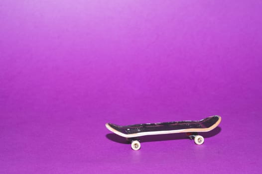 Small skateboard on purple background. tiny skate for fingers. fingerboard close up. copy space