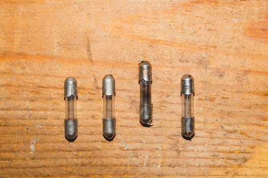 Row of fuses with burned out fuse on wooden background. safety device for overcurrent protection. protection of an electrical circuit
