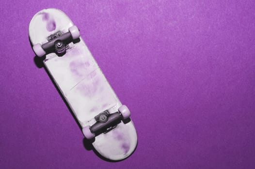 Small skateboard on purple background. tiny skate for fingers. fingerboard close up. copy space