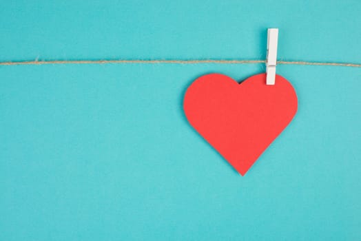 A heart hanging on a clothing line, blue colored background, empty copy space, symbol of love, valintine greeting card