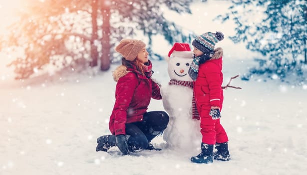 Mother and her little child playing in the winter park. Woman and boy making a snowman.