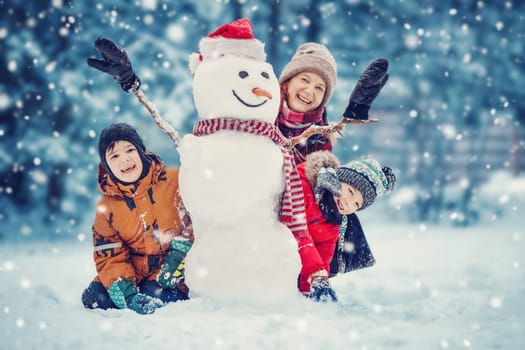Mother and her children playing in the winter park. Woman and boys making a snowman.