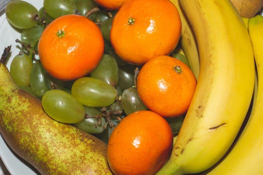 Ordinary fruit plate with natural looking fruits. fresh bananas, grapes, mandarins and pears