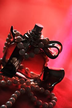 Bottle of perfume and pearls on red silk