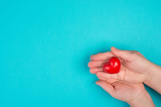 Woman is holding a red heart in her hand, blue colored background, copy space