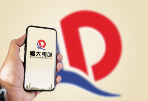 Guangzhou, China, October 2021: hand holding a phone with the Evergrande logo on the screen and the logo blurred in the background. Evergrande is the second largest property developer in China by sales