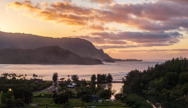 A vibrant aerial view of sunset clouds over the lush landscape of Hanalei Bay, framed by majestic mountains in Kauai, Hawaii.