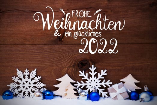 German Calligraphy Frohe Weihnachten Und Ein Glueckliches 2022 Means Merry Christmas And Happy 2022. Blue Christmas Decoration Like Tree, Gift And Ball. Wooden Background With Snow