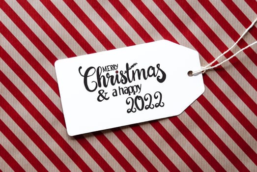 Label With English Calligraphy Merry Christmas And A Happy 2022. Red Wrapping Paper As Background