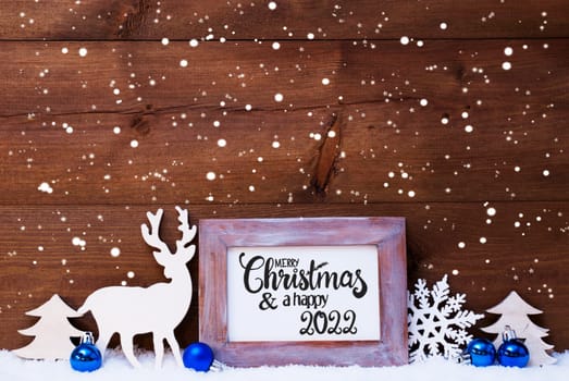 Frame With English Calligraphy Merry Christmas And A Happy 2022. Blue Christmas Decoration Like Ball, Tree And Deer. Wooden Background With Snow