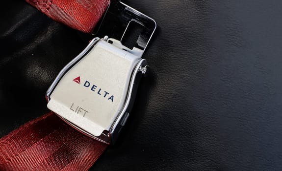 Atlanta, USA, October 2021: Red lap belt of an empty seat inside an airplane with the Delta Airlines logo printed on the metal. Delta is one of the major airlines of the United States