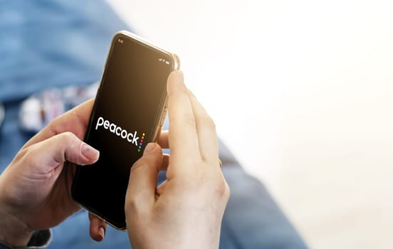 New York, USA, September 2021: Woman holding a smart phone with the Peacock TV mobile app on the screen. Peacock is an American video streaming service