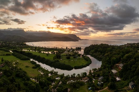 A vibrant aerial view of sunset clouds over the lush landscape of Hanalei Bay, framed by majestic mountains in Kauai, Hawaii.