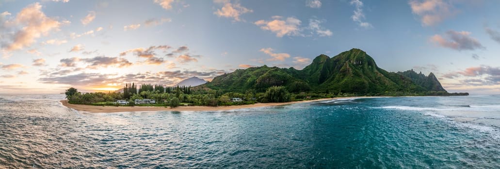Tunnels Beach panorama view from above at sunset, with the clear turquoise water and lush green mountains in the background