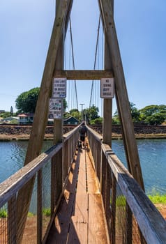 Hanapepe, Kauai - 2 February 2025: Man walking across the historic wooden swinging bridge across the river in Hanapepe