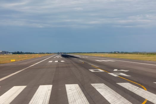 runway of airport with cloudy sky and print of wheels at the surface