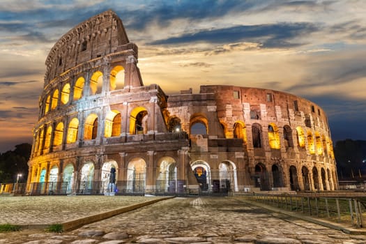 Illuminated Roman Coliseum under the clouds at sunrise, Italy.