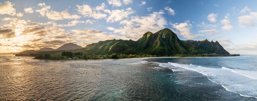Tunnels Beach panorama view from above at sunset, with the clear turquoise water and lush green mountains in the background