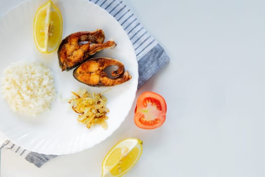 Fried fish with onions, rice and lemon lies on a plate, on a waffle towel and cutlery on a white background. High quality photo
