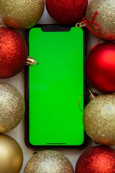 A phone with a green screen lies among the golden and red Christmas balls. High quality photo