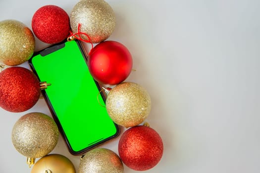 A phone with a green screen lies among the golden and red Christmas balls. High quality photo