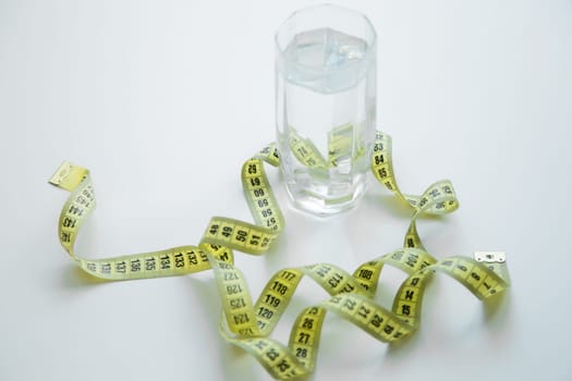 A green apple and a glass of water stand on a white background, they are entwined with a measuring tape. High quality photo