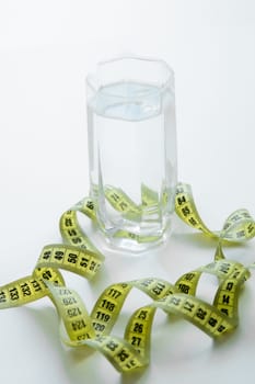 A glass of water is wrapped with a measuring tape on a white background. . High quality photo