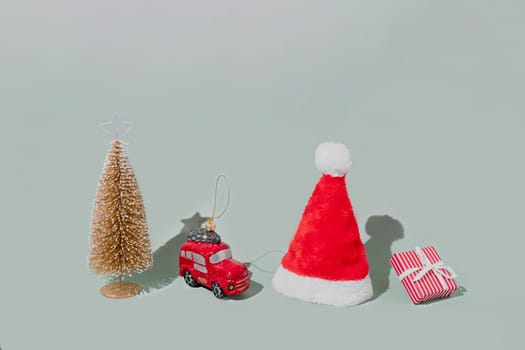 Gray background with Christmas or New Year symbol attribute objects and symbolic items concept. Pink gift box present with ribbon, small red taxi car toy, fir tree and red festive santa hap or cap
