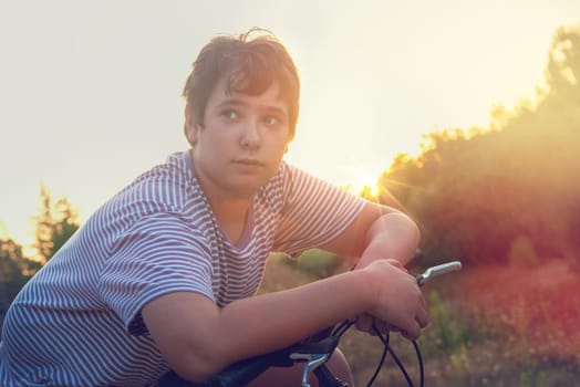 Happy boy posing in a bicycle outdoors at sunset