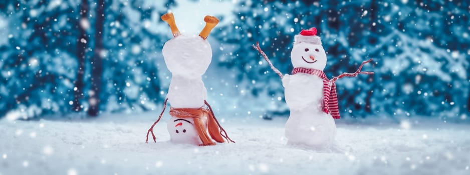 Cheerful snowmen standing in magical winter forest. Panoramic view of the beautiful background in snowy natural park in snowfall.