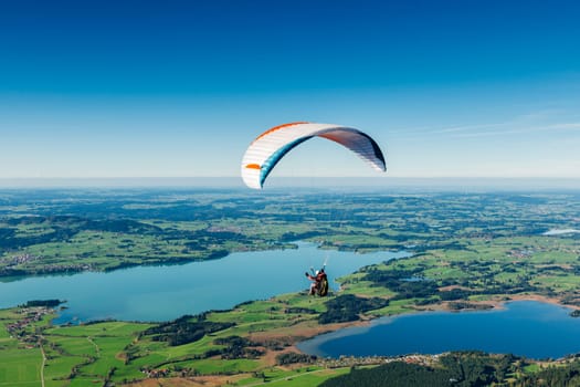 Paraglider pilots over a lake landscape in Bavaria in front of a blue sky and a wonderful panoramic view.