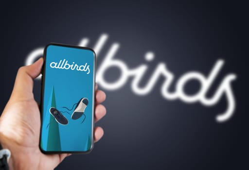 San Francisco, USA, October 2021: hand holding a phone with the Allbirds mobile app on the screen and the logo blurred on a blue background. Allbirds designs and sells footwear and apparel
