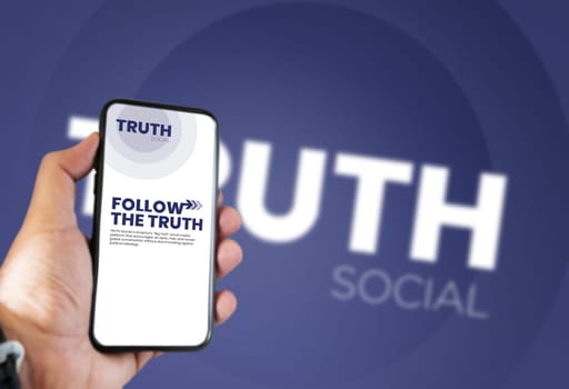 New York, USA, Oct 2021: hand holding a phone with the Truth Social mobile app on the screen and the logo blurred in the background. Truth Social is a social media platform launched by Donald Trump