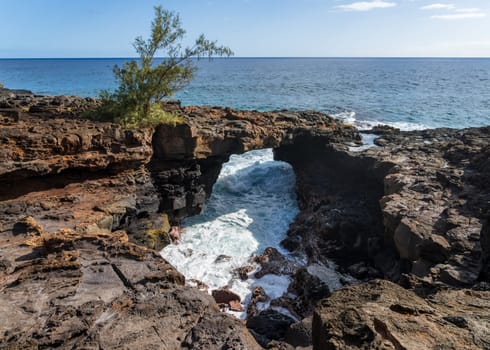 A natural lava arch provides a stunning contrast to the bright blue ocean at Poipu, Kauai, creating a beautiful coastal scene.