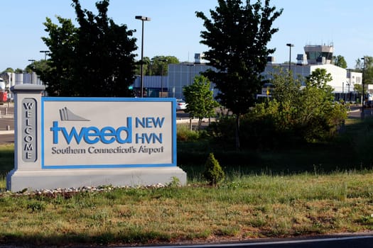 New Haven, CT, USA - May 27, 2021: Entrance sign to Tweed New Haven airport code, HVN, on a sunny evening with airport in back. Tweed New Haven airport entry sign with airport and a plane in background.