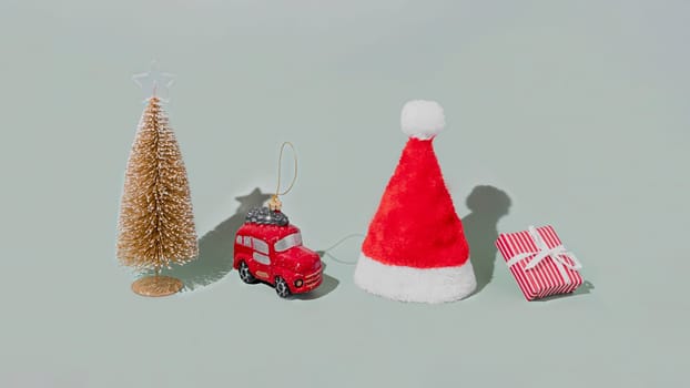Gray background with Christmas or New Year symbol attribute objects and symbolic items concept. Pink gift box present with ribbon, small red taxi car toy, fir tree and red festive santa hap or cap