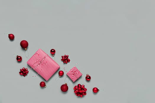 Gray background with two pink Christmas gift box presents, small red Christmas balls or sphere toys, ribbon bows for fir tree. Concept for festive sales, promotions, greeting card or invitation photo