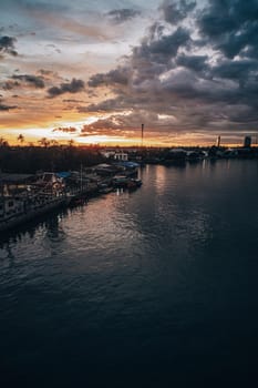 Panorama Cityscape at sunset with large river at foreground and storm clouds at background in Thailand.