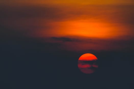 Beautiful sunset. Dramatic Fiery Sun Surrounded by Clouds During Sunset.  Vibrant orange red clouds are back lit by the sun.